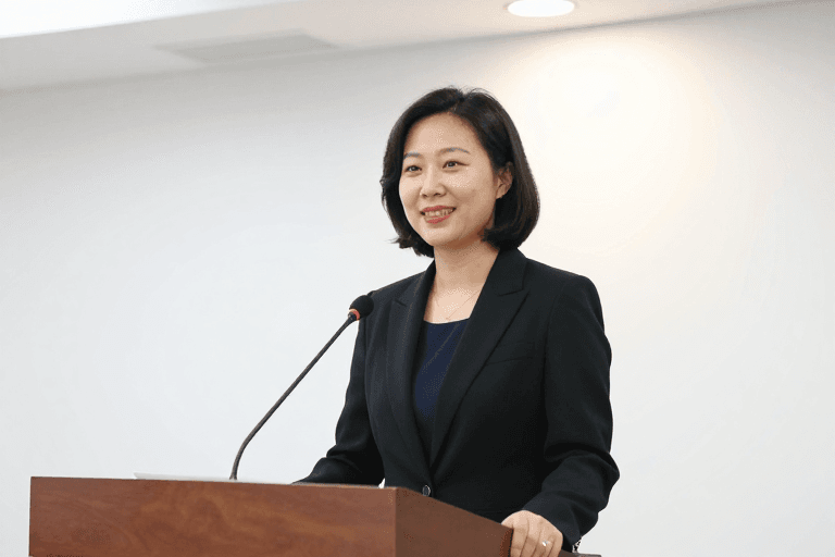 中性白平衡素材：专业亚洲女性讲师微笑面对镜头，商务演讲场景